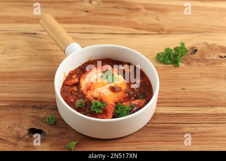 Shakshouka, plat d'œufs maison avec sauce tomate servi dans un bol en céramique blanc, petit déjeuner Moyen-Orient. Cuisine de confort Banque D'Images