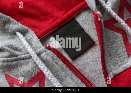 Étiquette noire vierge pour les vêtements d'entretien du linge sur fond de texture rouge et gris. Banque D'Images