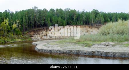 Érosion corrosion de la rive ronde sablonneuse d'une petite rivière Yakut du Nord dans la toundra sauvage du Nord dans une forêt pittoresque d'épinette. Banque D'Images