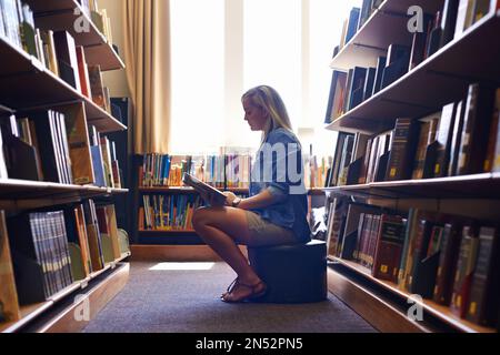 Shes toujours à la recherche d'un bon endroit pour étudier. Une jeune étudiante de la bibliothèque. Banque D'Images