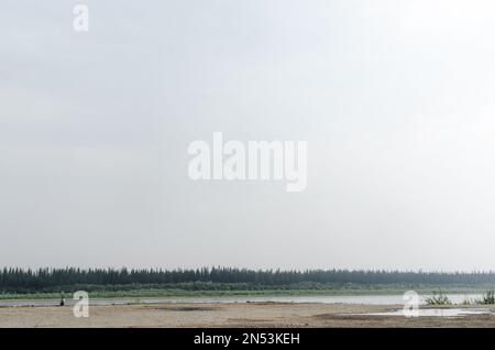 Fille voyageur assis sur le bord de l'ancien quai sur les rives de la rivière vilyu avec des forêts d'épinette et la toundra de Yakutia dans l'extrême nord de Ru Banque D'Images