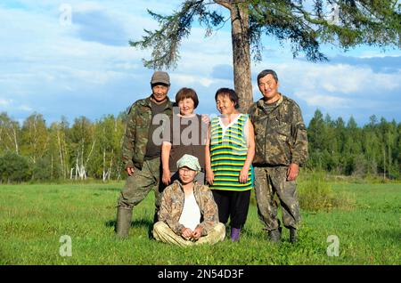 Deux couples Yakut asiatiques âgés hommes et femmes avec une jeune fille assise sur l'herbe posent pour une photo de famille dans un champ près d'un arbre. Banque D'Images