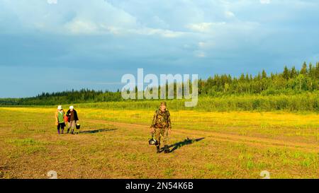 Un yakut souriant se promène devant deux amies discutant au soleil sur la rive sauvage en pierre de la Viluy du Nord au coucher du soleil. Banque D'Images