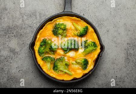 Omelette végétarienne saine avec brocoli vert dans une poêle en fonte noire avec fourche et couteau vue sur fond de béton gris en pierre Banque D'Images