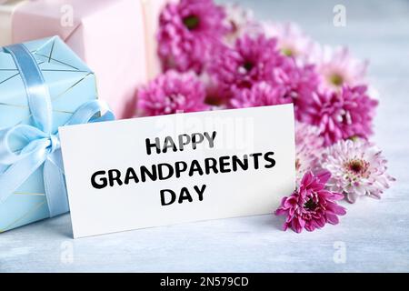 Belles fleurs, boîtes-cadeaux et carte avec phrase Happy Grandparents Day sur table grise Banque D'Images
