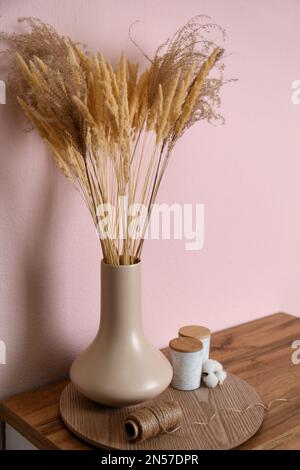Vase avec plantes séchées décoratives sur table en bois près du mur rose. Design intérieur Banque D'Images