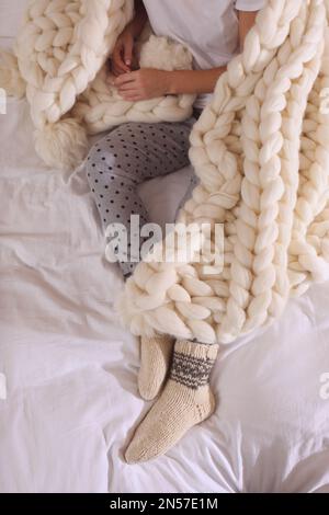 Femme couverte de tissu écossais tricoté sur le lit, gros plan Banque D'Images