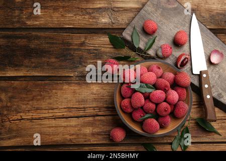 Fruits de lychee mûrs frais et couteau sur table en bois, plat. Espace pour le texte Banque D'Images