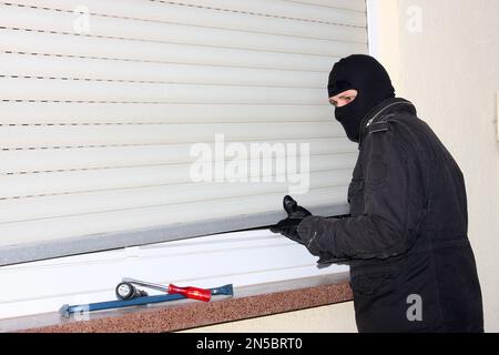 cambrioleur avec un tournevis, un pied de biche et une lampe de poche sur un store à roulettes Banque D'Images