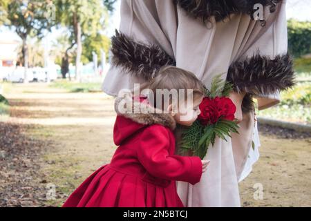 Une jolie petite fille blanche de race blanche sentant un bouquet de roses tenu par sa mère Banque D'Images