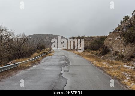 Chaussée en lambeaux le long de la falaise avec des taches de neige et un ciel couvert dans la campagne du Nouveau-Mexique Banque D'Images