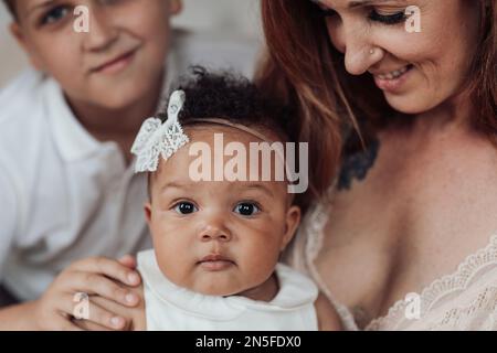 Famille mixte de race avec fils blancs et fille naissante passer du temps ensemble dans l'appartement confortable. Homme afro-américain avec sa femme à la peau juste ki Banque D'Images