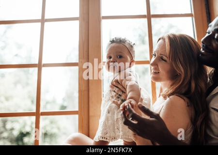 Famille de race mixte avec la peau sombre bébé fille passer du temps ensemble utiliser la fenêtre claire dans l'appartement Snug. Homme afro-américain sa femme de peau équitable an Banque D'Images