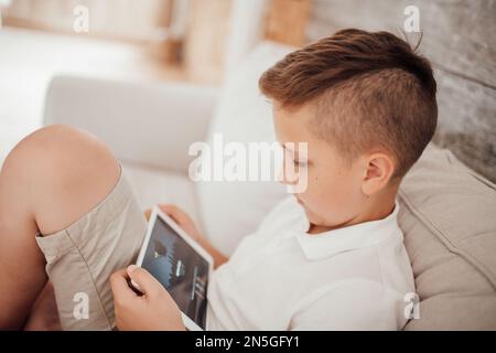 Gen Z boy utilisant la technologie sans fil à l'appartement dans des tons neutres intérieur. Portrait authentique et sincère d'un jeune adolescent avec une émotion positive avec Mo Banque D'Images