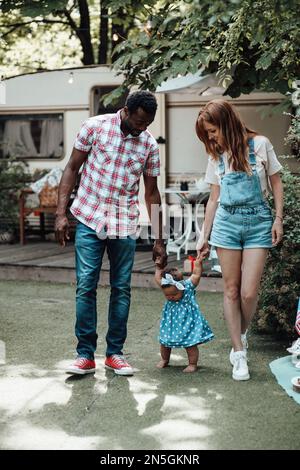 Famille de race mixte avec fille à la peau foncée passer du temps ensemble et enseigner à bébé à marcher en plein air. Homme afro-américain, sa femme, soutient Banque D'Images