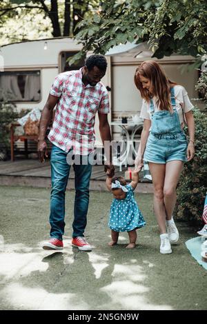 Famille de race mixte avec fille à la peau foncée passer du temps ensemble et enseigner à bébé à marcher en plein air. Homme afro-américain, sa femme, soutient Banque D'Images