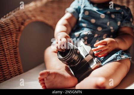 Petite fille en robe bleue à pois a une émotion positive assise sur une chaise de canne et ombre sur le visage. Bébé afro-américain détend un Banque D'Images