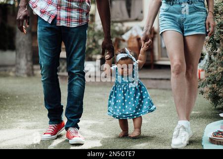 Famille de race mixte avec fille à la peau foncée passer du temps ensemble et enseigner à bébé à marcher en plein air. Homme afro-américain, sa femme, soutient Banque D'Images