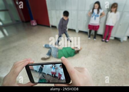 La main de la personne filmant deux écoliers combattant dans le couloir scolaire avec téléphone mobile, Bavière, Allemagne Banque D'Images