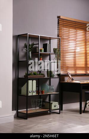 Étagères avec décor différent, livres et plantes de maison près du mur gris dans la chambre. Design intérieur Banque D'Images