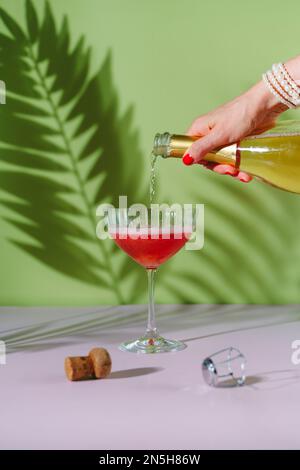 Une main de femme avec une manucure rouge verse du champagne dans un verre. Banque D'Images