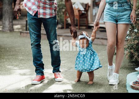 Famille de race mixte avec fille à la peau foncée passer du temps ensemble et enseigner à bébé à marcher en plein air. Homme afro-américain, sa femme, soutient Banque D'Images