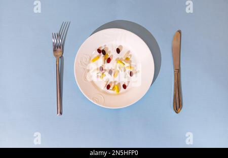 Comprimés, pilules et capsules sur une plaque en porcelaine blanche. La barre de coupe est équipée d'une plaque, d'une fourchette, d'un couteau. Arrière-plan bleu et lumineux. Médecine et vitamines inst Banque D'Images