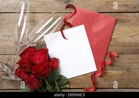 Composition de pose à plat avec carte de vœux vierge, verres et roses sur table en bois. Célébration de la Saint-Valentin Banque D'Images