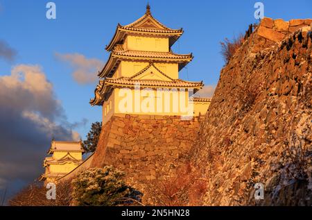 La lumière de l'heure d'or frappe l'ancien château japonais au sommet d'un mur de pierre Banque D'Images