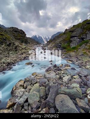 La rivière alpine coule sur des pierres de montagnes avec des glaciers et de la neige en Altai en Sibérie derrière les nuages pluvieux pendant la journée. Cadre vertical. Banque D'Images