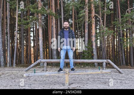 Hipster homme barbu adulte séjournant dans une aire de jeux dans la forêt. Concept de la santé, de l'harmonie et de l'équilibre. Banque D'Images