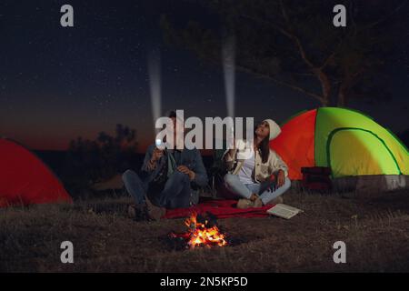 Couple avec des lampes torches près de feu de camp la nuit. Saison de camping Banque D'Images