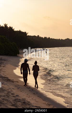 Maldives plage - un couple sur un long voyage de vacances à pied au bord de l'eau sur une plage de sable au coucher du soleil, Rasdhoo Atoll, les Maldives, l'océan Indien Asie Banque D'Images