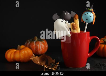 Différents types de gâteau dans une tasse décorée comme des monstres sur une table noire. Halloween Banque D'Images