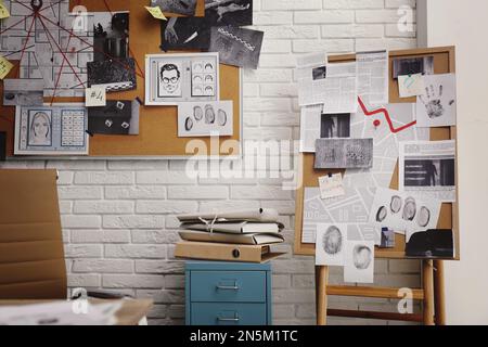 Tableaux avec photos de scènes de crime et cartes près du mur de briques blanches dans le bureau de détective Banque D'Images