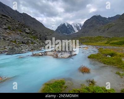 Le cours d'eau turquoise alpin coule parmi les pierres orange des montagnes avec des glaciers en Altai en Sibérie pendant la journée. Banque D'Images