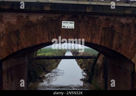 Cours d'eau entre les champs cultivés vu d'un pont par une journée nuageux dans la campagne italienne en hiver Banque D'Images