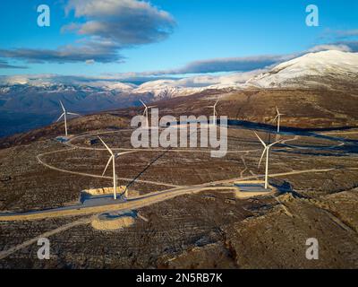 Moulins à vent sur les collines pendant le coucher du soleil. Énergies renouvelables, énergies vertes. Montagnes en arrière-plan avec de la neige. Énergie éolienne et écologique. Banque D'Images