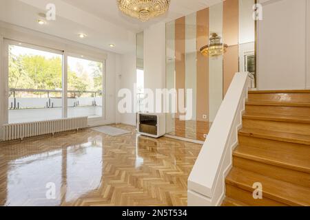 Salon d'un appartement de style loft avec une grande terrasse avec fenêtres en aluminium, parquet ciré, escaliers en bois et une murale miroir bicolore Banque D'Images