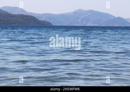 Vue sur mer bleue et île de montagne à l'horizon dans la brume. Surface de l'eau, fond pour les voyages et les vacances Banque D'Images