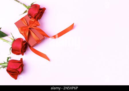 Carte de voeux pour la Saint-Valentin, la fête des mères et l'anniversaire. Roses rouges et boîte cadeau avec noeud en ruban satiné Banque D'Images