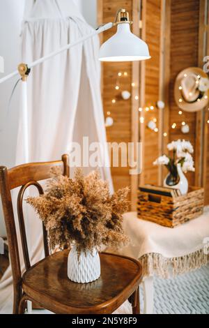 Cette chambre blanche et beige est décorée dans un style scandinave et boho. Pampas herbe dans le bouquet, chaise vintage, lampe blanche, confortable et doux Banque D'Images