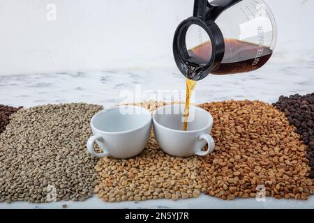 Une tasse de café frais sur la table du comptoir de cuisine et un arrière-plan flou. Pile de grains de café, pot fraîchement préparé et tasse gros plan. Tasse à café remplie de Banque D'Images