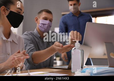 Se comporte avec des masques de protection en utilisant de l'assainisseur pour les mains au bureau. Réunion d'affaires pendant la pandémie de COVID-19 Banque D'Images