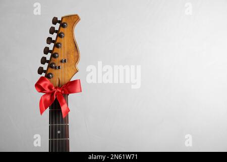 Guitare avec arc rouge sur fond clair, espace pour le texte. Musique de Noël Banque D'Images