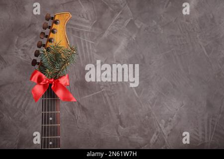 Guitare avec branche de sapin et noeud rouge sur fond gris, espace pour le texte. Musique de Noël Banque D'Images