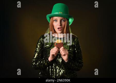 Une jeune femme rouge choquée avec un cookie sur fond sombre. St. Fête de la Patrick Banque D'Images