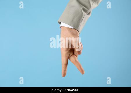 Homme d'affaires imitant marcher avec la main sur fond bleu clair, gros plan. Mouvement du doigt Banque D'Images