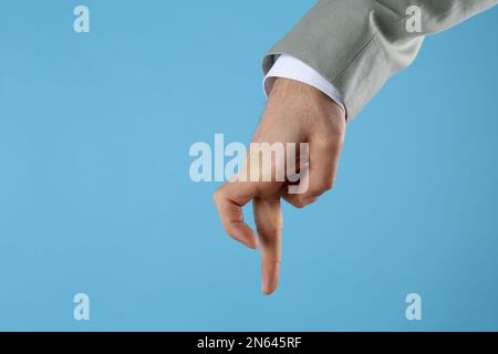 Homme d'affaires imitant marcher avec la main sur fond bleu clair, gros plan. Mouvement du doigt Banque D'Images