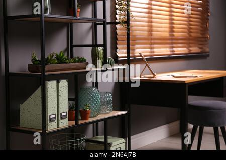 Étagères avec décoration différente et plantes de maison près de la table dans la chambre. Design intérieur Banque D'Images